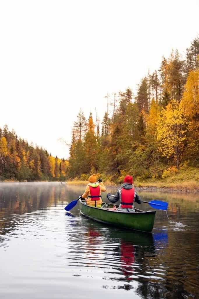 2 people canoeing through the river between 2 forests