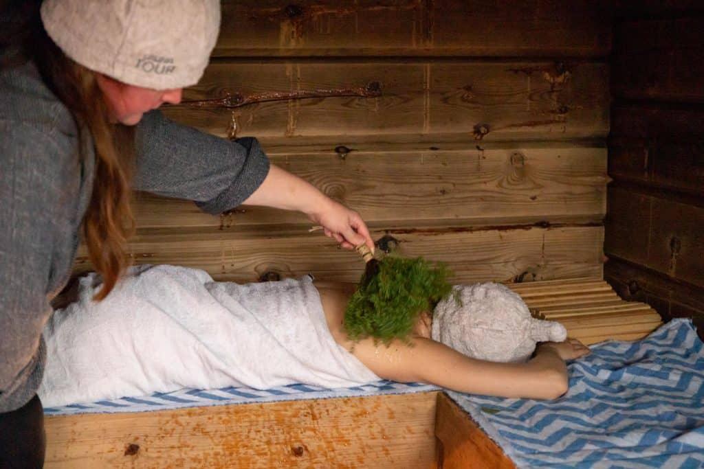 a woman using the sauna while being whisked with branches