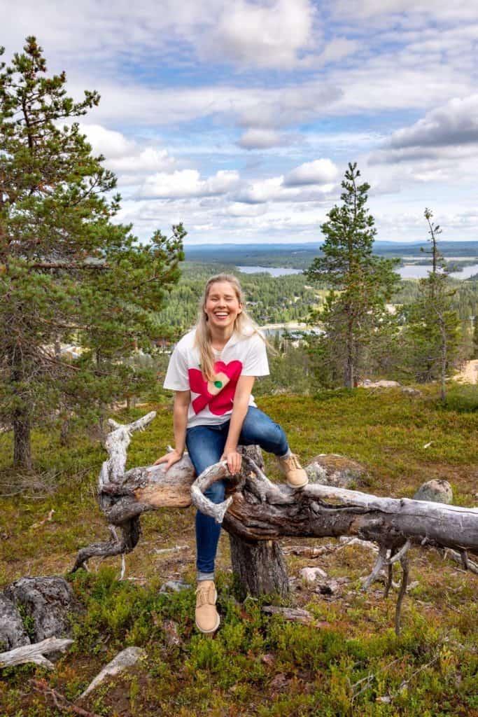 a woman sitting on a tree with lakes and trees in the background